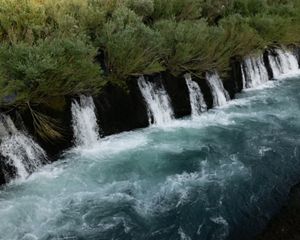 Blue river water cascades and froths over a natural wall of rock.