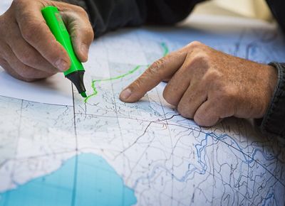 A close up of a hand highlighting a road along a map.